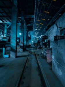 Blue-lit factory interior in Unnao, UP, India. Industrial feel with machinery and rail tracks in view.
